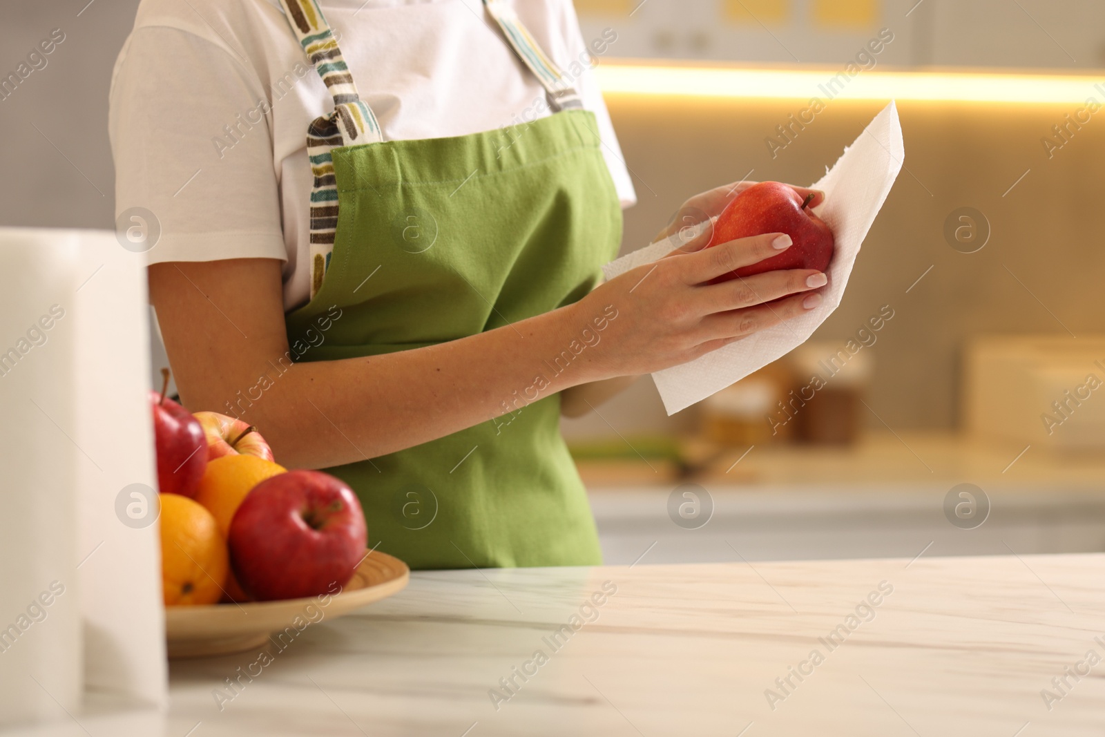 Photo of Woman wiping apple with paper towel at white marble table in kitchen, closeup