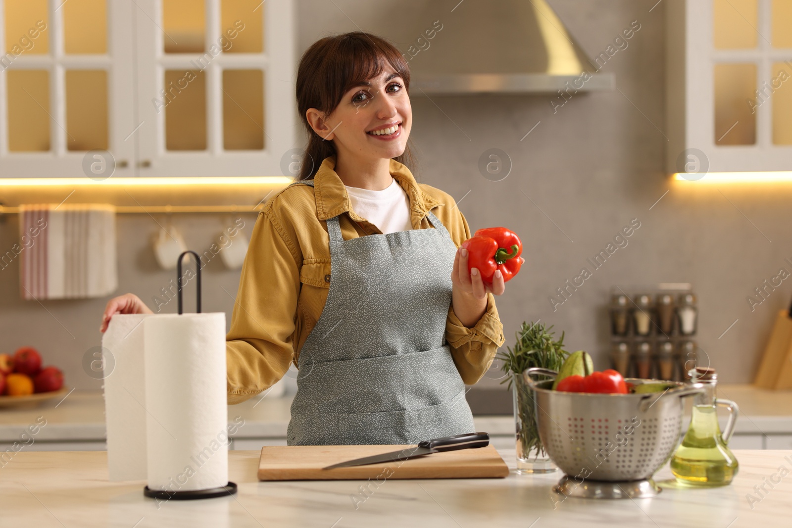 Photo of Woman with bell pepper using paper towels at white marble table in kitchen