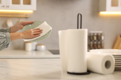 Photo of Woman wiping plate with paper towel at white marble table in kitchen, closeup