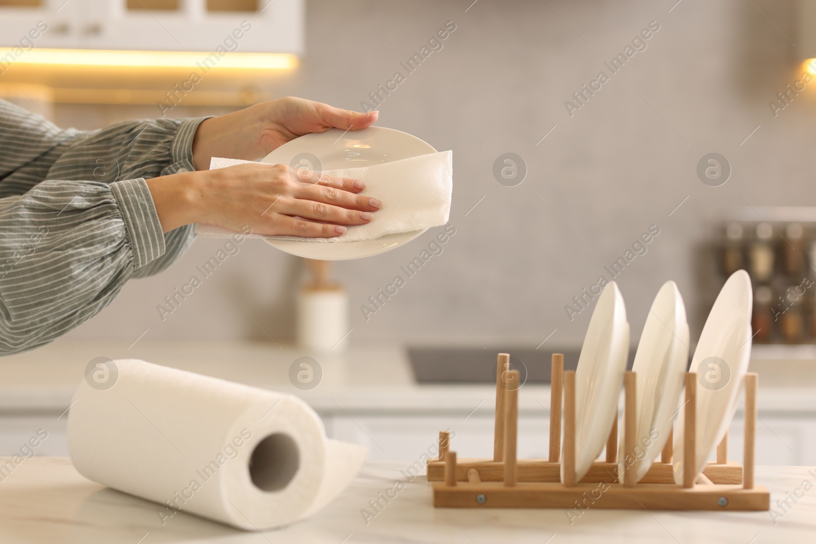 Photo of Woman wiping plate with paper towel at white marble table in kitchen, closeup