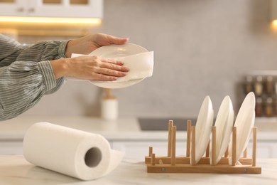 Photo of Woman wiping plate with paper towel at white marble table in kitchen, closeup