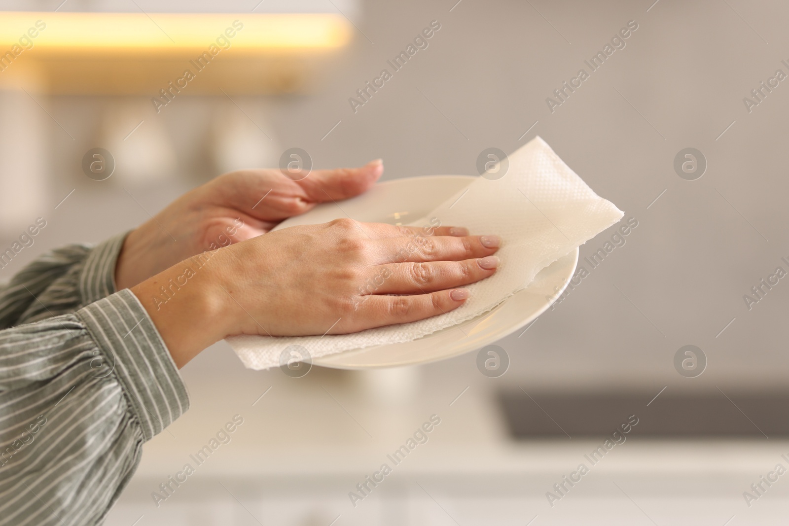 Photo of Woman wiping plate with paper towel in kitchen, closeup