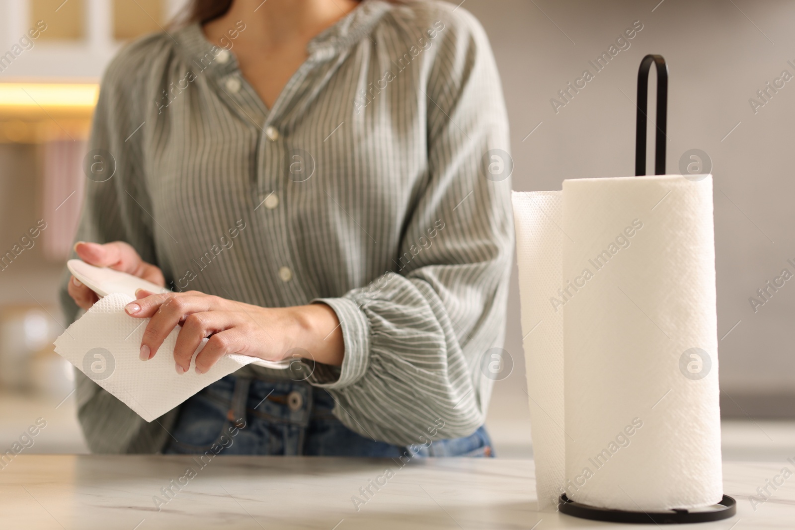 Photo of Woman wiping plate with paper towel at white marble table in kitchen, closeup