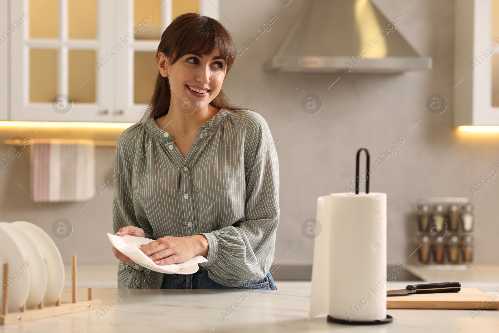 Photo of Woman wiping plate with paper towel at white marble table in kitchen