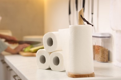 Photo of Woman cutting vegetables at white countertop in kitchen, focus on rolls of paper towels