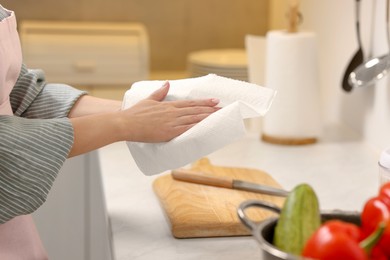 Photo of Woman wiping hands with paper towel in kitchen, closeup