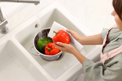 Woman wiping bell pepper with paper towel in kitchen, above view