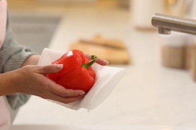 Photo of Woman wiping bell pepper with paper towel in kitchen, closeup