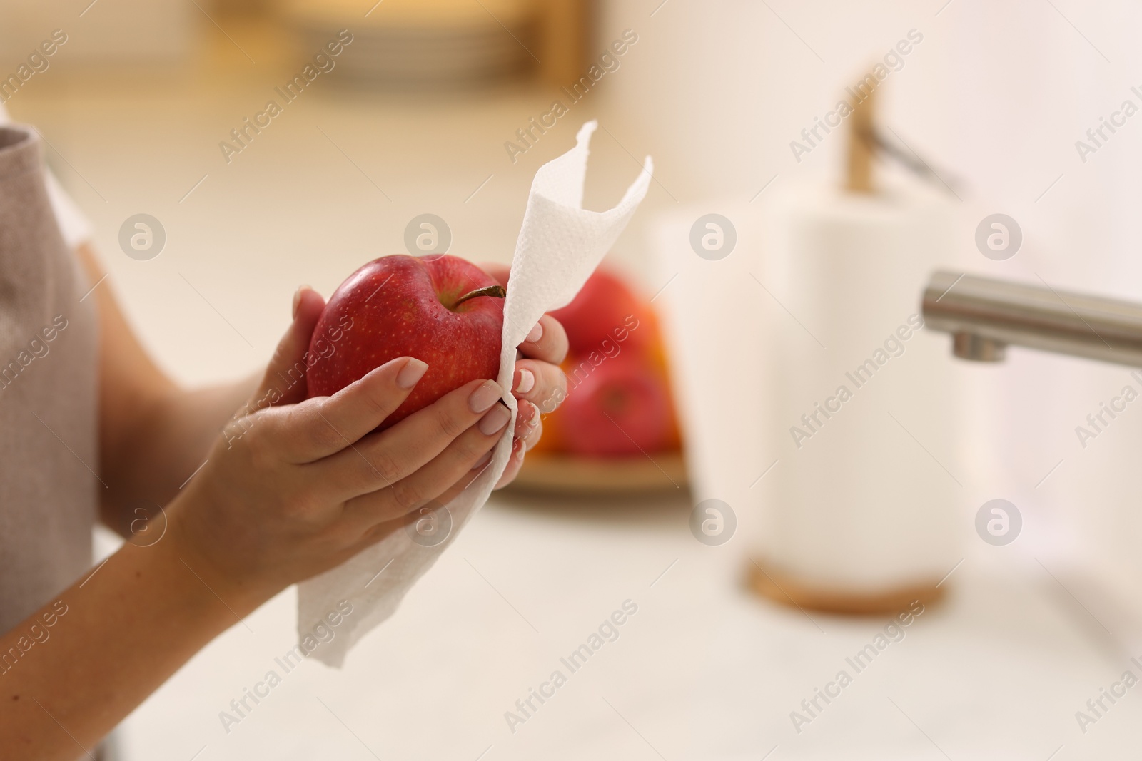 Photo of Woman wiping apple with paper towel in kitchen, closeup