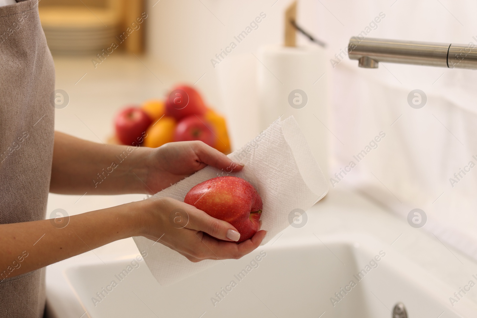 Photo of Woman wiping apple with paper towel above sink in kitchen, closeup