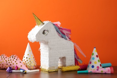 Photo of Bright pinata in shape of unicorn and party accessories on table against orange background