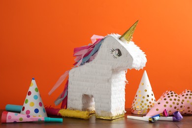 Photo of Bright pinata in shape of unicorn and party accessories on table against orange background