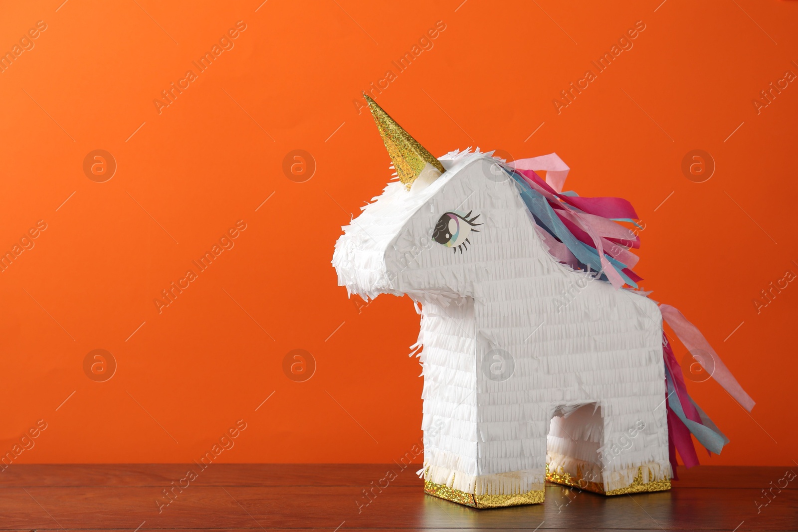 Photo of Bright pinata in shape of unicorn on table against orange background. Space for text