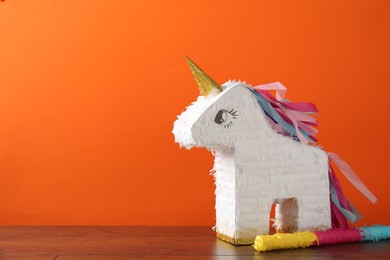 Photo of Bright pinata in shape of unicorn and stick on table against orange background. Space for text