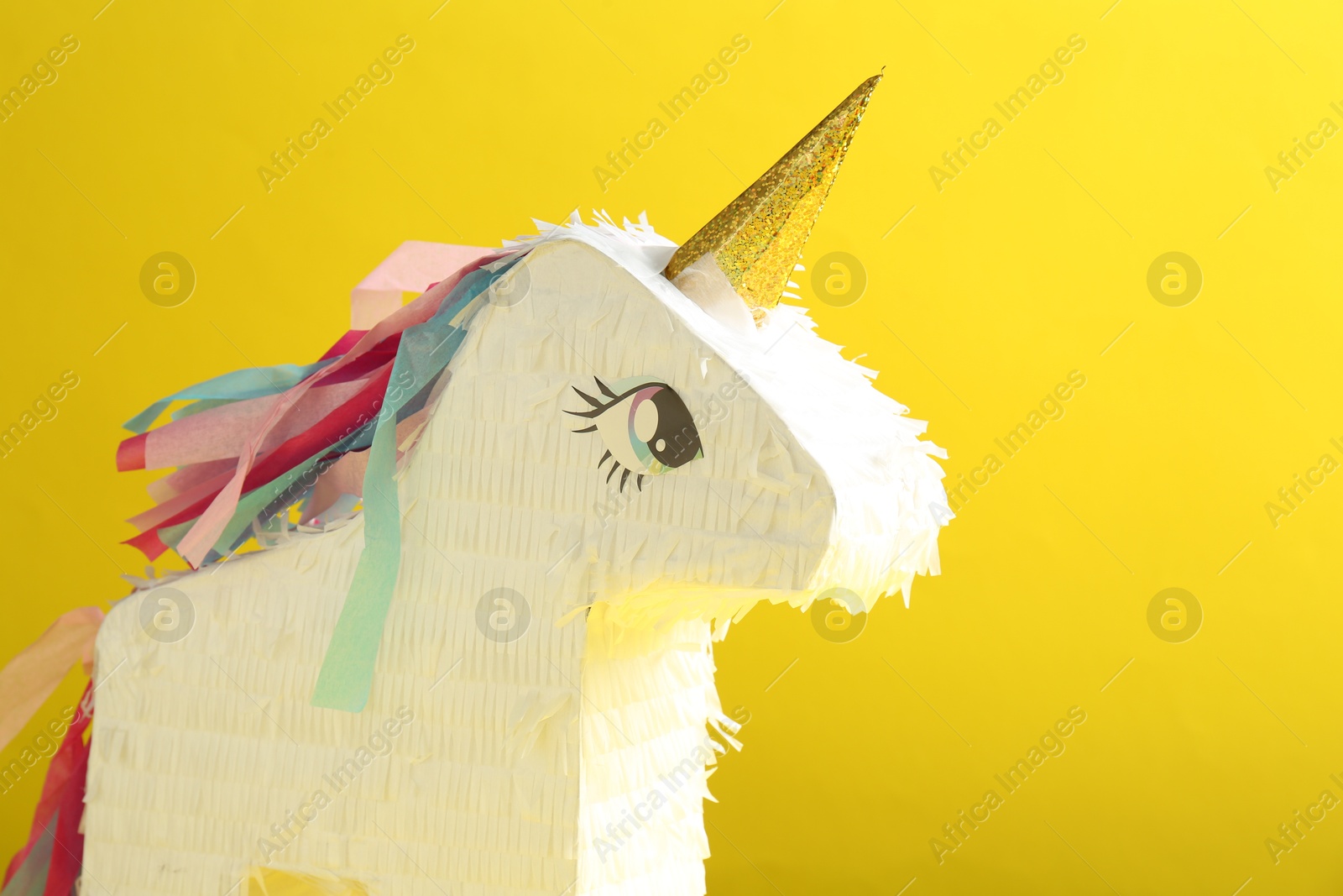 Photo of Bright pinata in shape of unicorn on yellow background