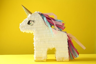 Photo of Bright pinata in shape of unicorn on yellow background