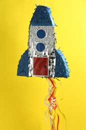 Photo of Bright pinata in shape of spaceship hanging on yellow background