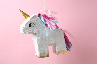 Photo of Bright pinata in shape of unicorn hanging on pink background