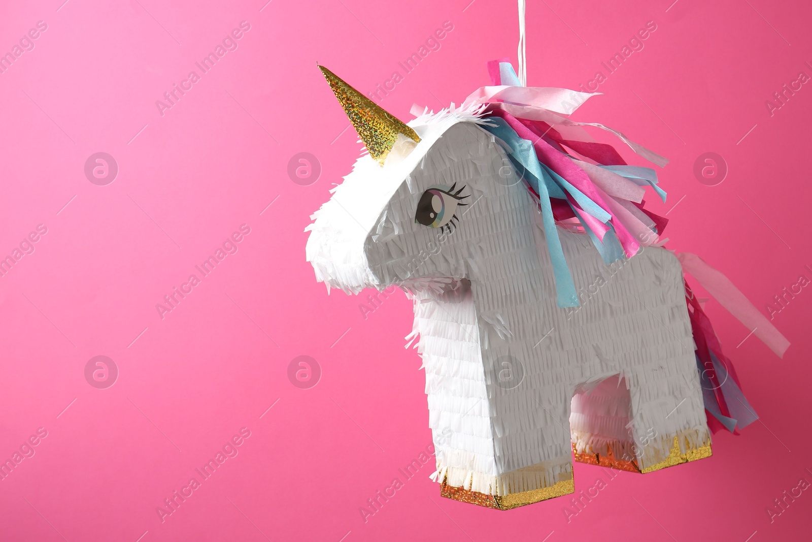 Photo of Bright pinata in shape of unicorn hanging on pink background