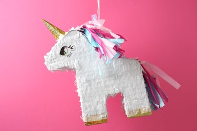 Photo of Bright pinata in shape of unicorn hanging on pink background