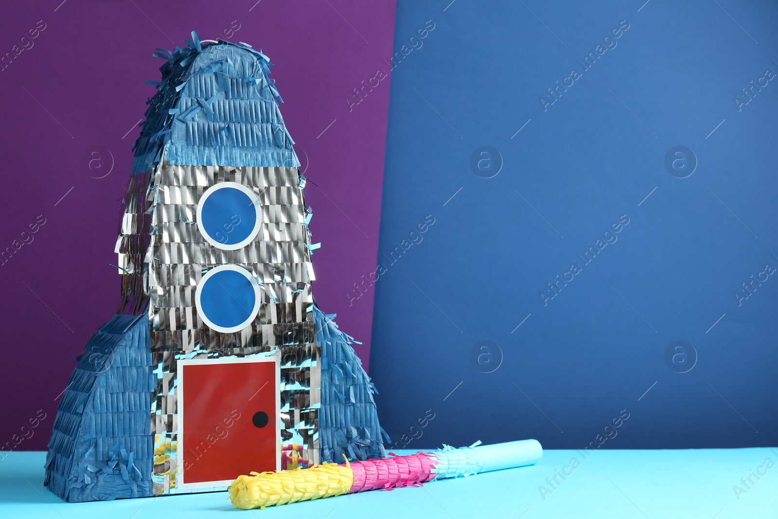 Photo of Bright pinata in shape of spaceship and stick on color background. Space for text