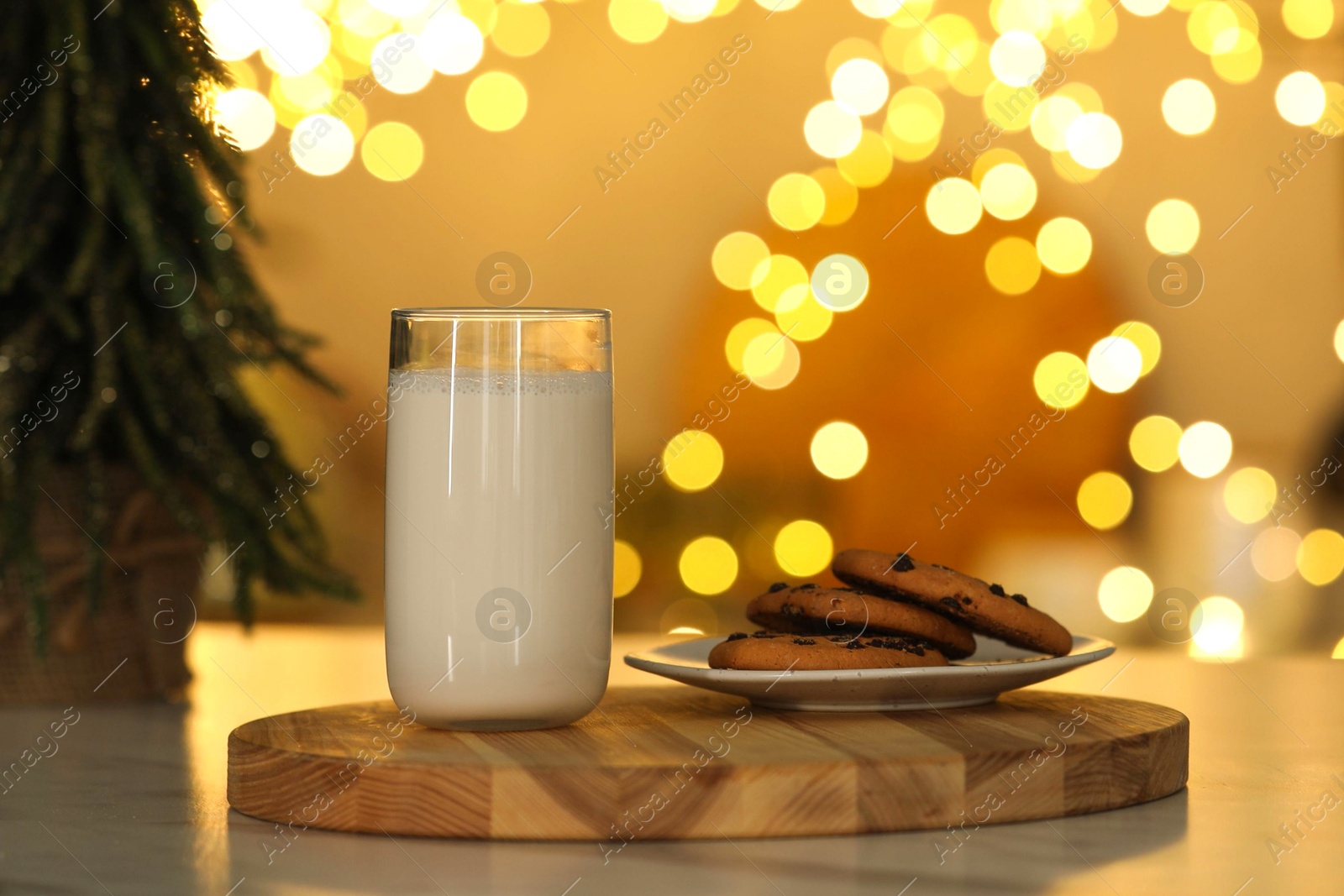 Photo of Glass of milk and tasty chocolate chip cookies on table against blurred Christmas lights. Bokeh effect