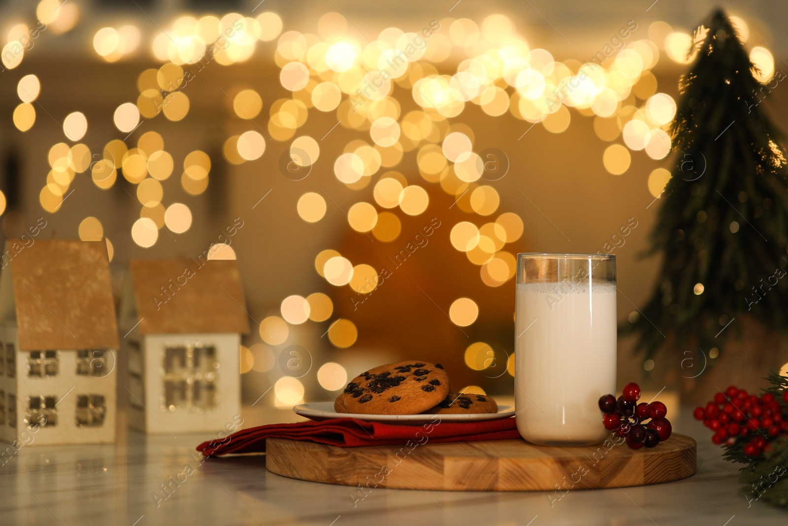 Photo of Glass of milk, tasty chocolate chip cookies and Christmas decor on table against blurred lights. Bokeh effect