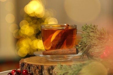 Photo of Cup of tea with lemon and cinnamon stick on table against blurred Christmas lights. Bokeh effect