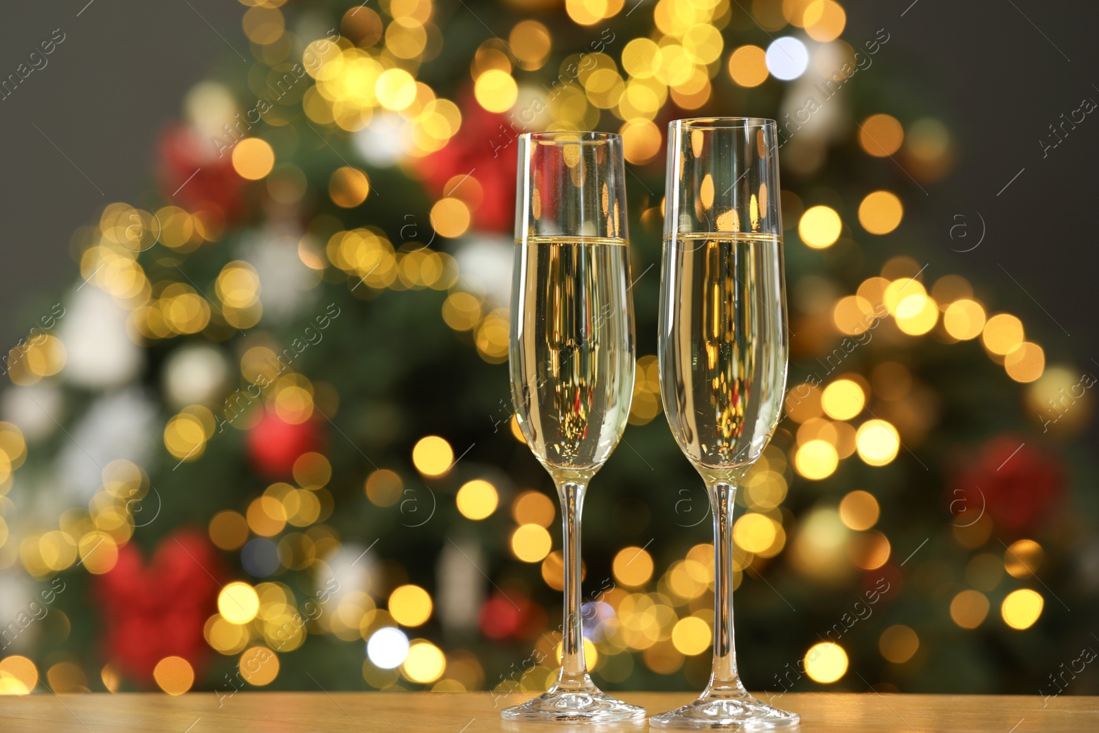 Photo of Champagne in glasses on wooden table against blurred Christmas lights, space for text. Bokeh effect