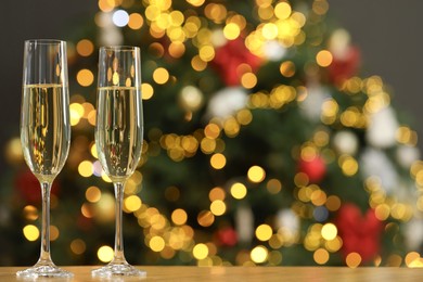 Photo of Champagne in glasses on wooden table against blurred Christmas lights, space for text. Bokeh effect