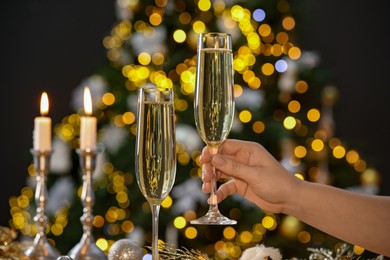 Photo of Woman with glass of champagne against blurred Christmas lights, closeup. Bokeh effect