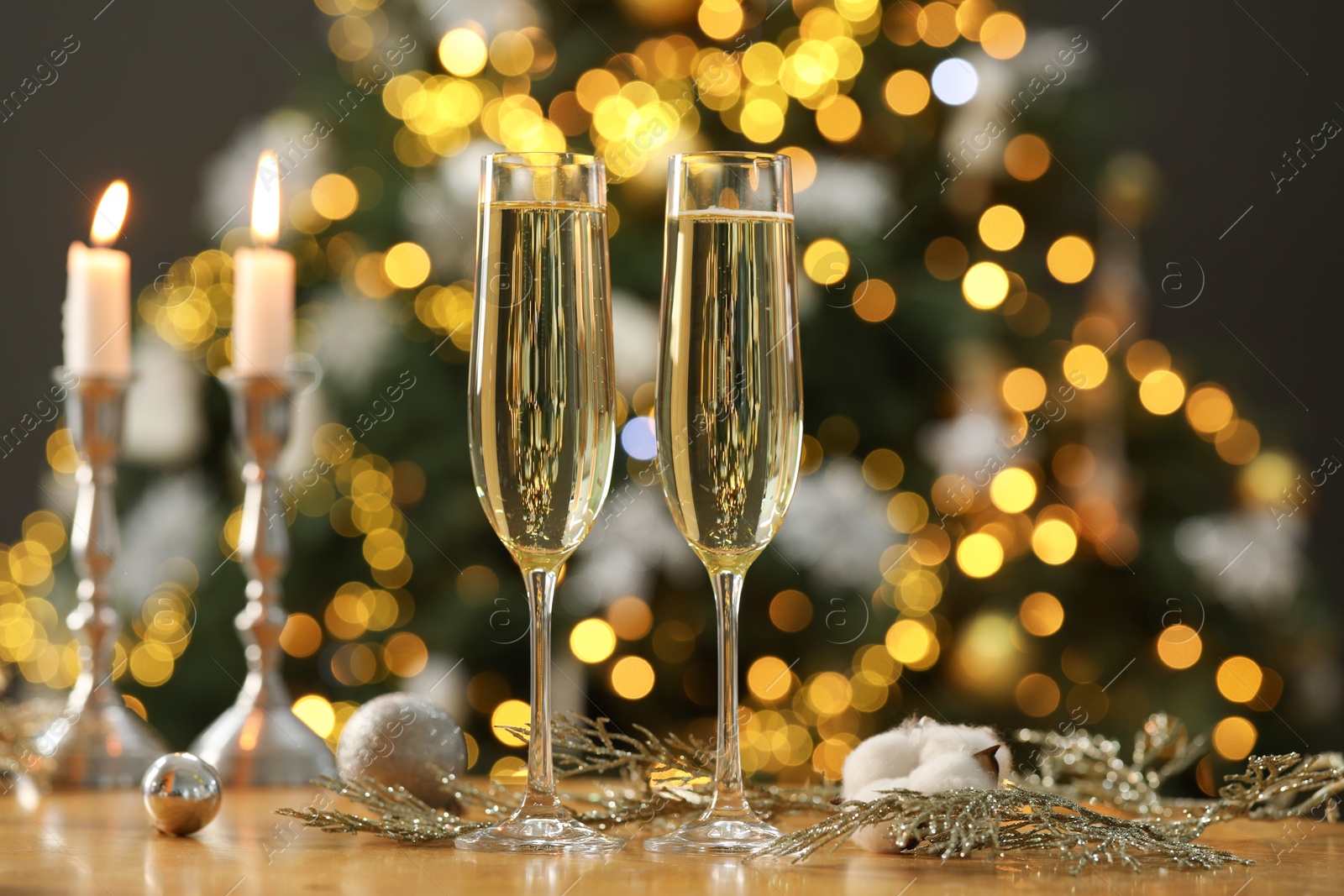 Photo of Champagne in glasses and decor on table against blurred Christmas lights, bokeh effect