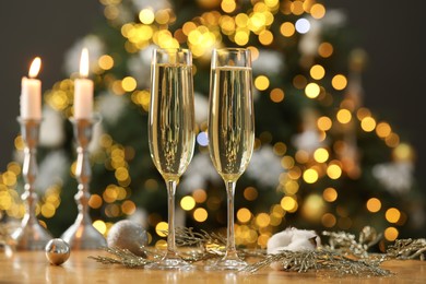 Photo of Champagne in glasses and decor on table against blurred Christmas lights, bokeh effect