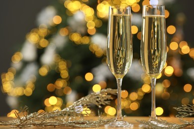 Photo of Champagne in glasses and decor on table against blurred Christmas lights, space for text. Bokeh effect