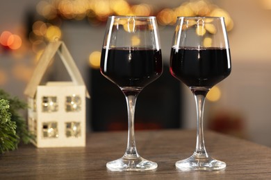 Photo of Red wine in glasses on wooden table against blurred Christmas lights, bokeh effect