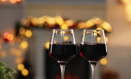 Photo of Red wine in glasses against blurred Christmas lights, closeup. Bokeh effect