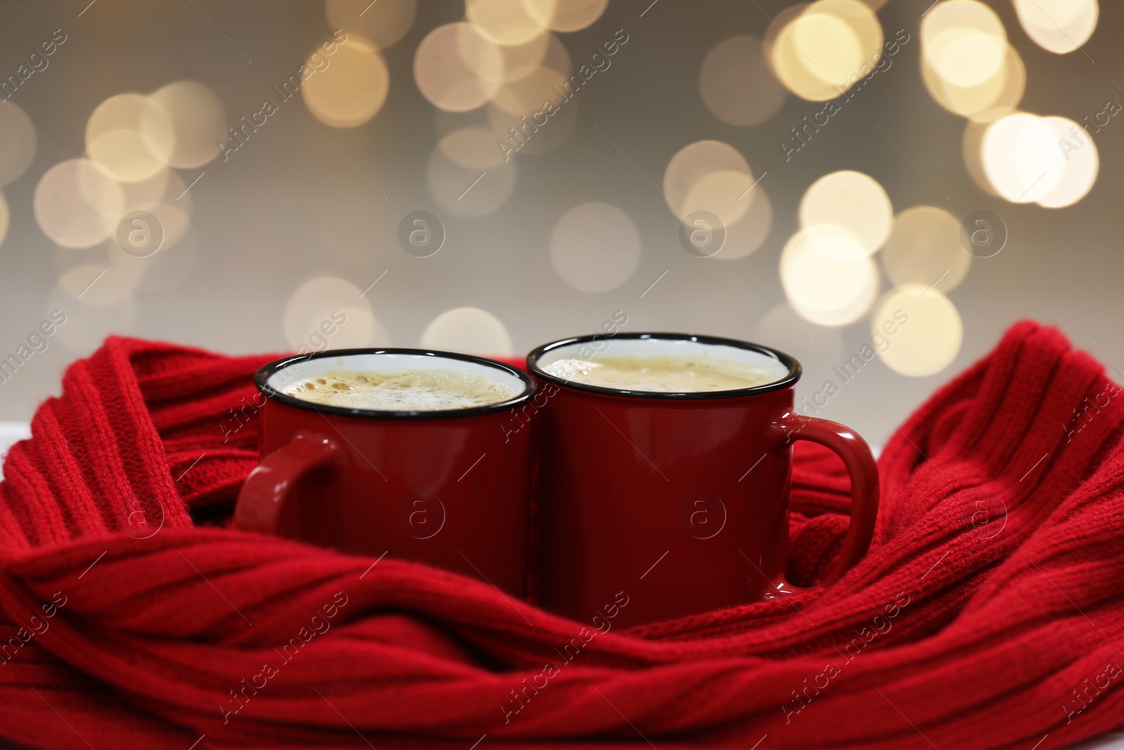 Photo of Tasty cocoa in cups and red scarf on table indoors