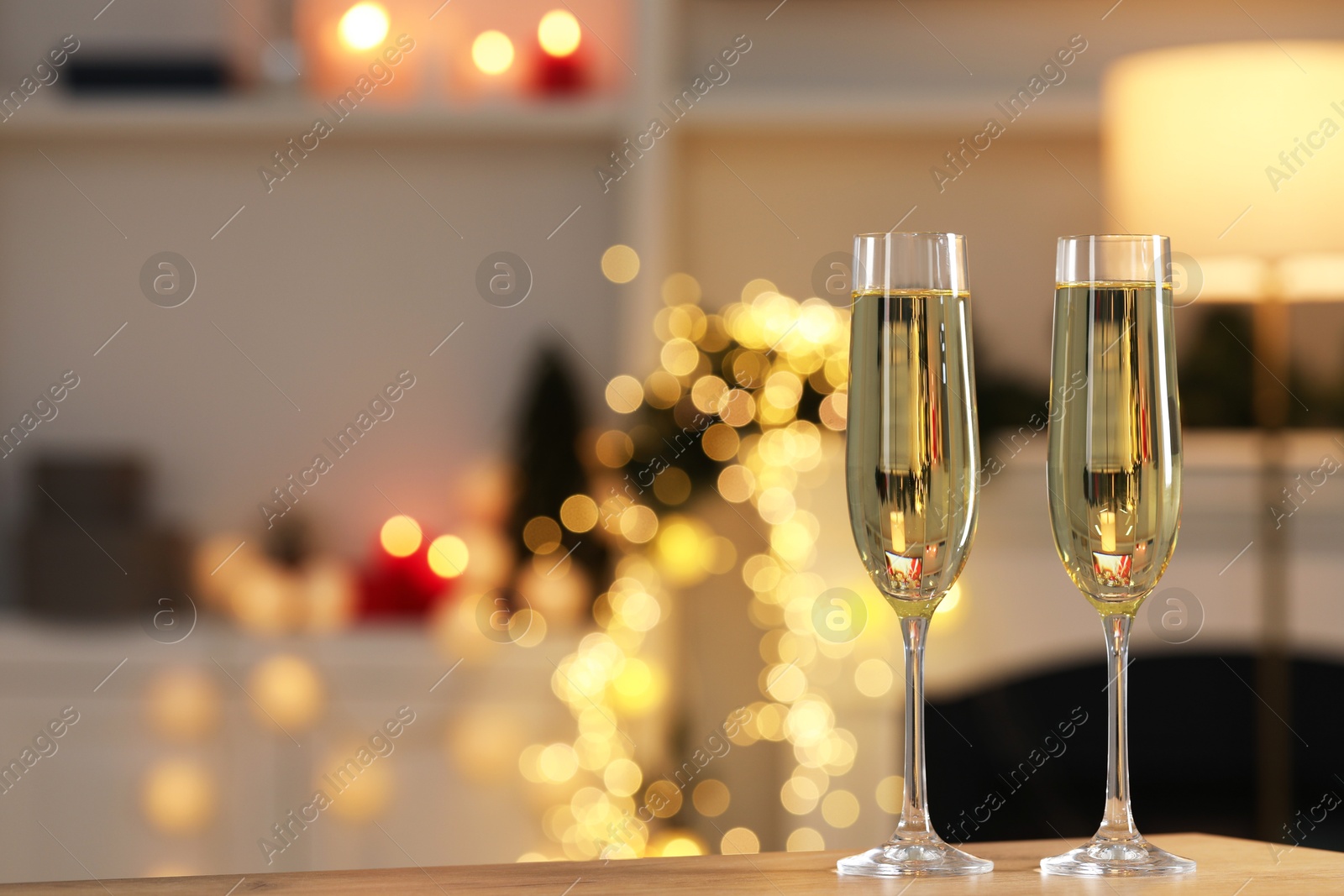 Photo of Champagne in glasses on wooden table against blurred Christmas lights, space for text. Bokeh effect