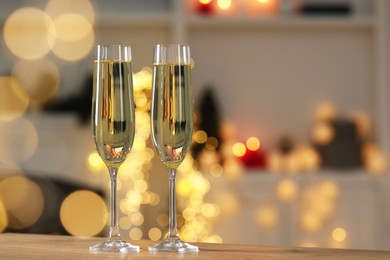 Photo of Champagne in glasses on wooden table against blurred Christmas lights, space for text. Bokeh effect