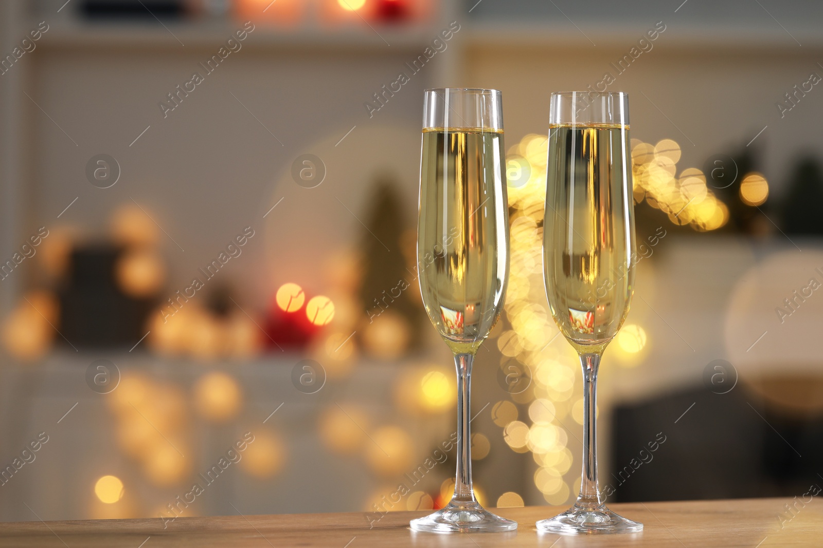 Photo of Champagne in glasses on wooden table against blurred Christmas lights, space for text. Bokeh effect