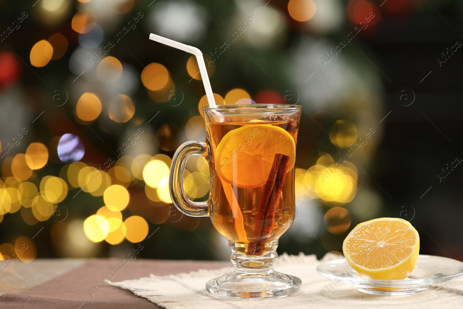 Photo of Hot tea with lemon and cinnamon on table against blurred Christmas lights, space for text. Bokeh effect