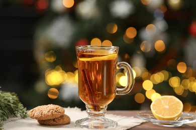 Photo of Hot tea with lemon, cinnamon and tasty cookies on table against blurred Christmas lights, bokeh effect