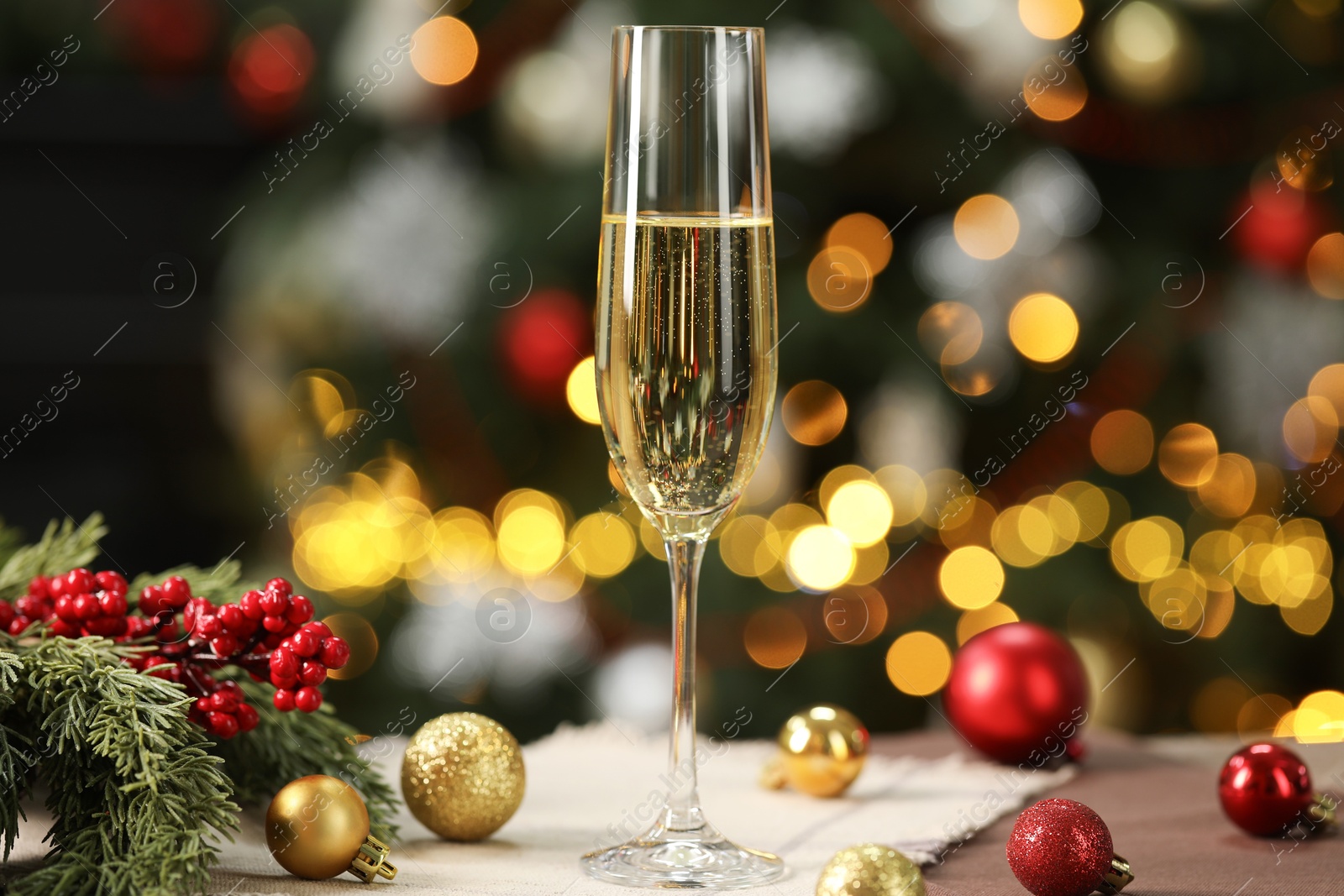 Photo of Champagne in glass and decor on table against blurred Christmas lights, bokeh effect