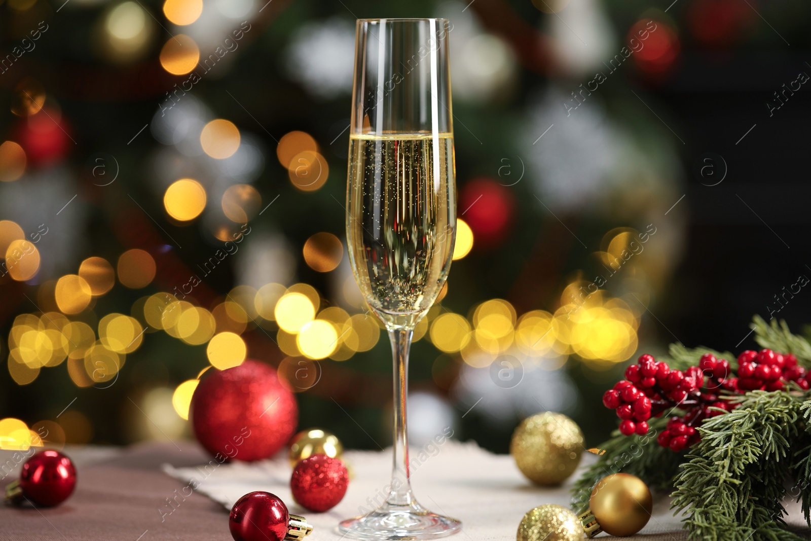 Photo of Champagne in glass and decor on table against blurred Christmas lights, bokeh effect