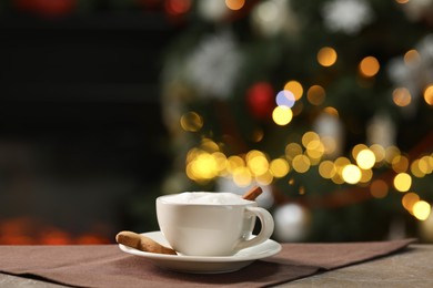 Photo of Aromatic coffee in cup and tasty cookie on table against blurred Christmas lights, space for text. Bokeh effect