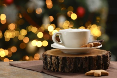 Photo of Aromatic coffee in cup and tasty cookies on table against blurred Christmas lights, space for text. Bokeh effect