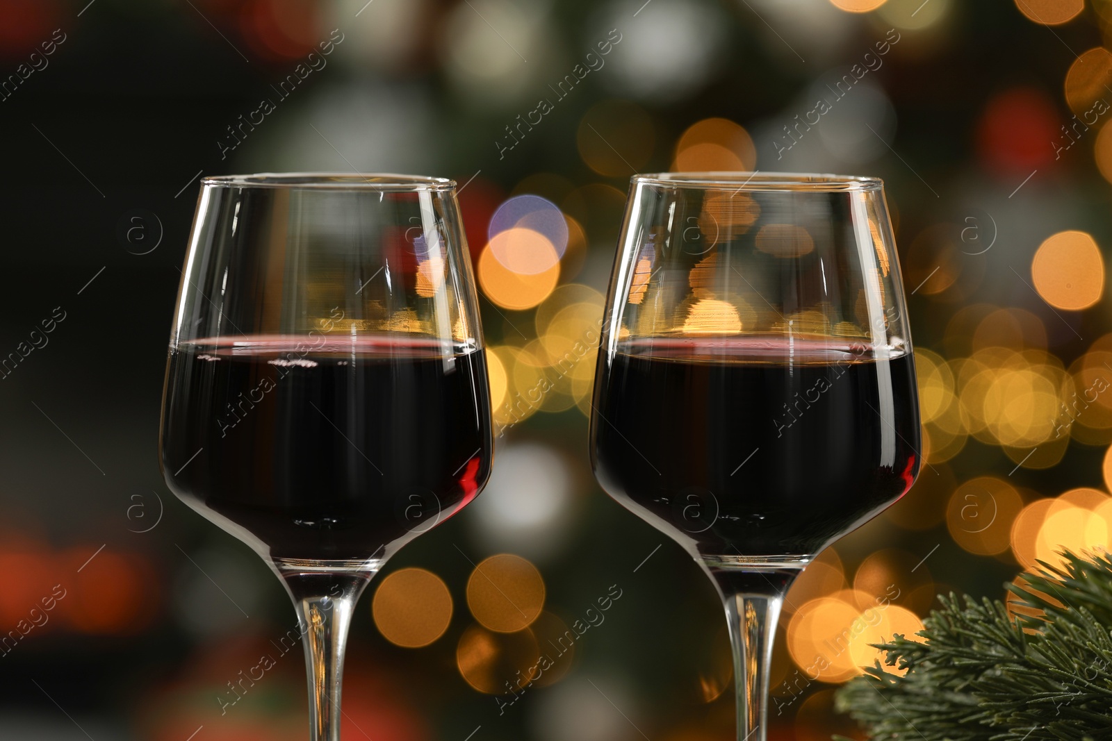 Photo of Red wine in glasses against blurred Christmas lights, closeup. Bokeh effect