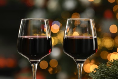 Photo of Red wine in glasses against blurred Christmas lights, closeup. Bokeh effect