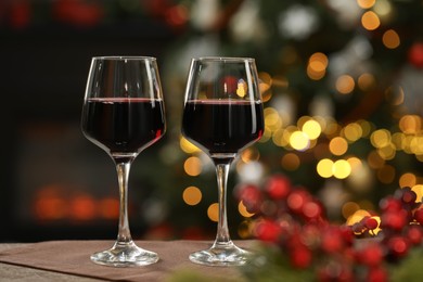 Photo of Red wine in glasses on table against blurred Christmas lights, space for text. Bokeh effect