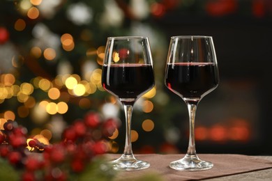 Photo of Red wine in glasses on table against blurred Christmas lights, space for text. Bokeh effect